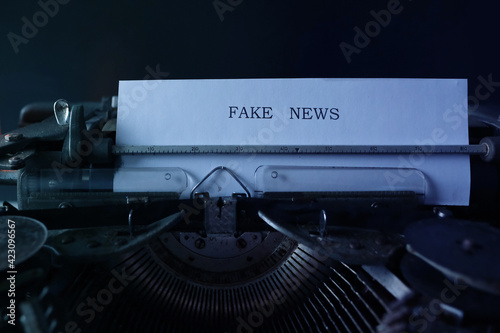 old typewriter on table, words fake news are printed on paper in large size, candle is burning, retro style, concept of information hoax in social media, misleading, exposing deception