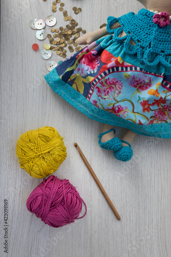 Brown sewing needle and yarn balls next to a handcrafted multicolor doll over a wooden gray background. photo