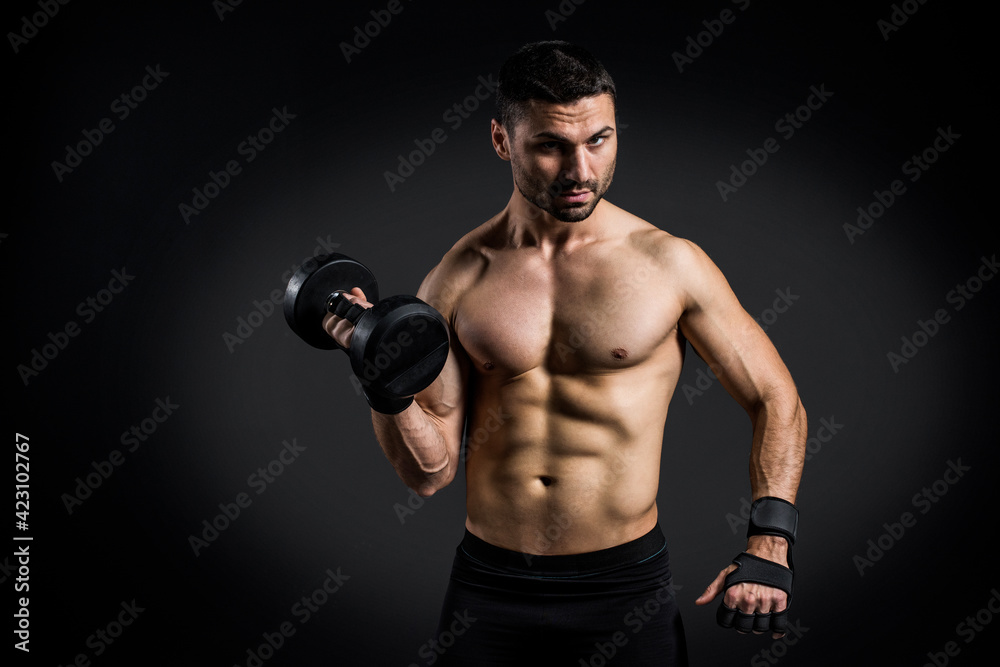 Young power athletic man doing exercise on biceps with heavy dumbbells in gym on black background. Strength and motivation.