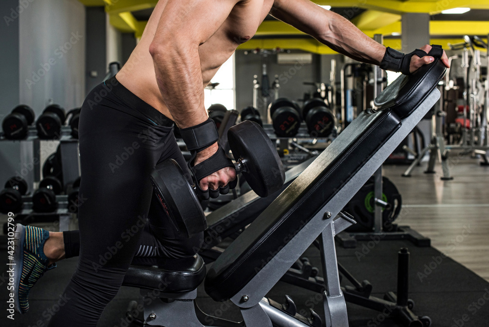 Young power athletic man doing exercise on biceps with heavy dumbbells in gym. Strength and motivation.