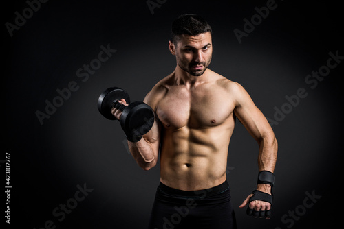 Young power athletic man doing exercise on biceps with heavy dumbbells in gym on black background. Strength and motivation.