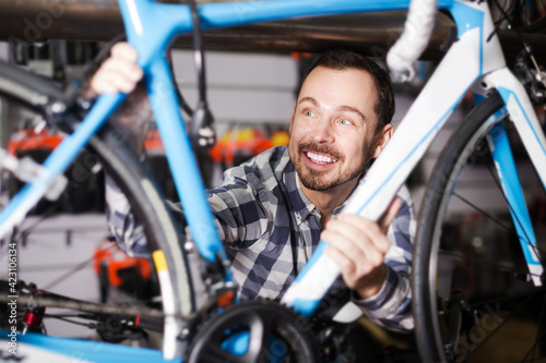Young cheerful man looks at bicycle frame in sports store