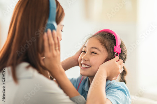 Happy daughter and mother listening music with headphones at home
