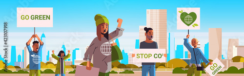 environmental activists holding posters go green save planet strike concept protesters campaigning to protect earth demonstrating against global warming portrait cityscape background horizontal