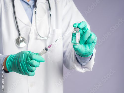 A doctor holding a vaccine bottle and syringe while standing on a gray background. Vaccine for immunization, and treatment from virus infection. Concept of medical and the fight against the virus