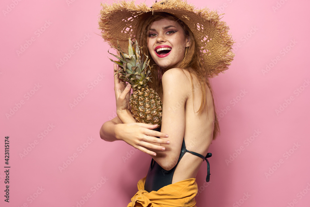 woman in beach hat pineapple exotic swimsuit pink background