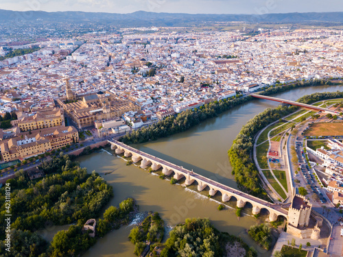 Aerial panoramic view of modern Cordoba cityscape on banks of Guadalquivir River with ancient pedestrian Roman Bridge and Mosque -Cathedral, Spain..