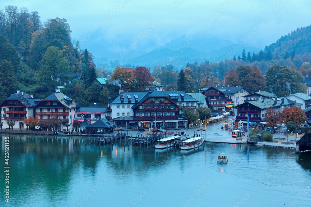 Sightseeing boats cruising on Konigssee ( King's Lake ) with lakeside hotels, resorts and boathouses at foggy misty dusk ~ Beautiful fall scenery of Bavarian countryside in Berchtesgaden Germany