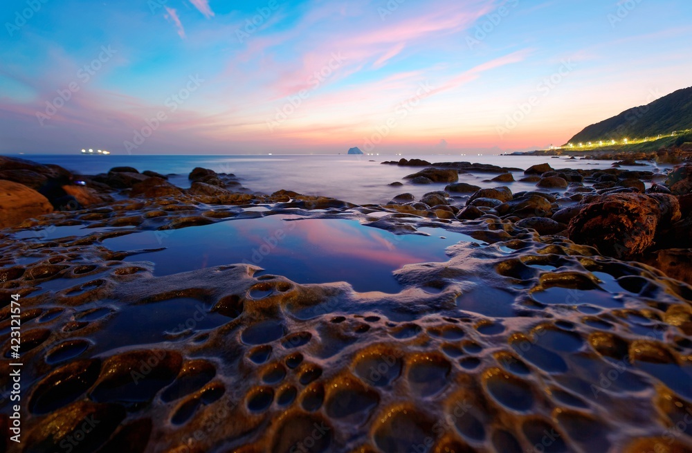 Naklejka premium Beautiful scenery of sunrise by rocky coast in northern Taiwan with reflection of golden sunlight on smooth sea water (long exposure effect) The famous attraction 