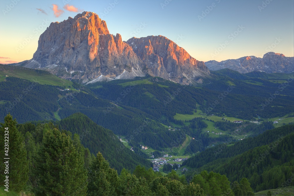 Sunset scenery of rugged Sassolungo-Sassopiatto mountains with alpenglow & a village in green grassy valley in Col Raiser, Val Gardena, Dolomiti National Park, South Tyrol, Italy, Europe (in Ortisei)