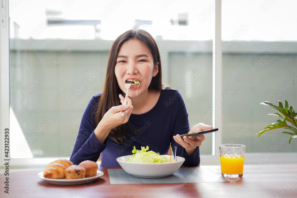 Young asian woman eating healthy salad with fresh vegetable on wellness lifestyle and looking on smartphone Young asian woman eating healthy salad with fresh vegetable on wellness lifestyle and looking on smartphone