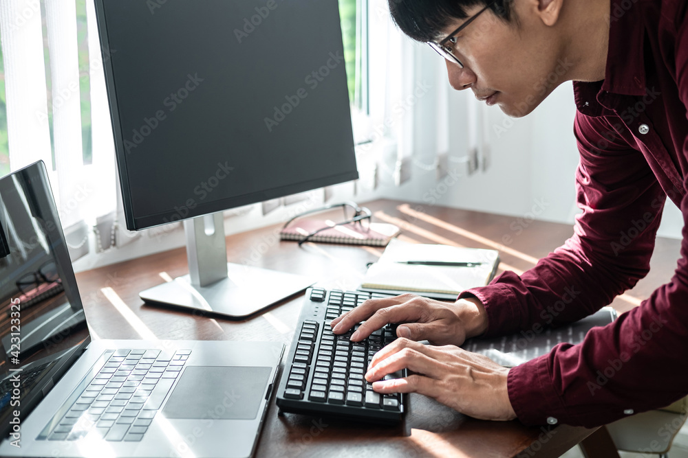 Asian man programmer looking on screen laptop to typing code data with keyboard about website and applications Asian man programmer looking on screen laptop to typing code data with keyboard about website and applications
