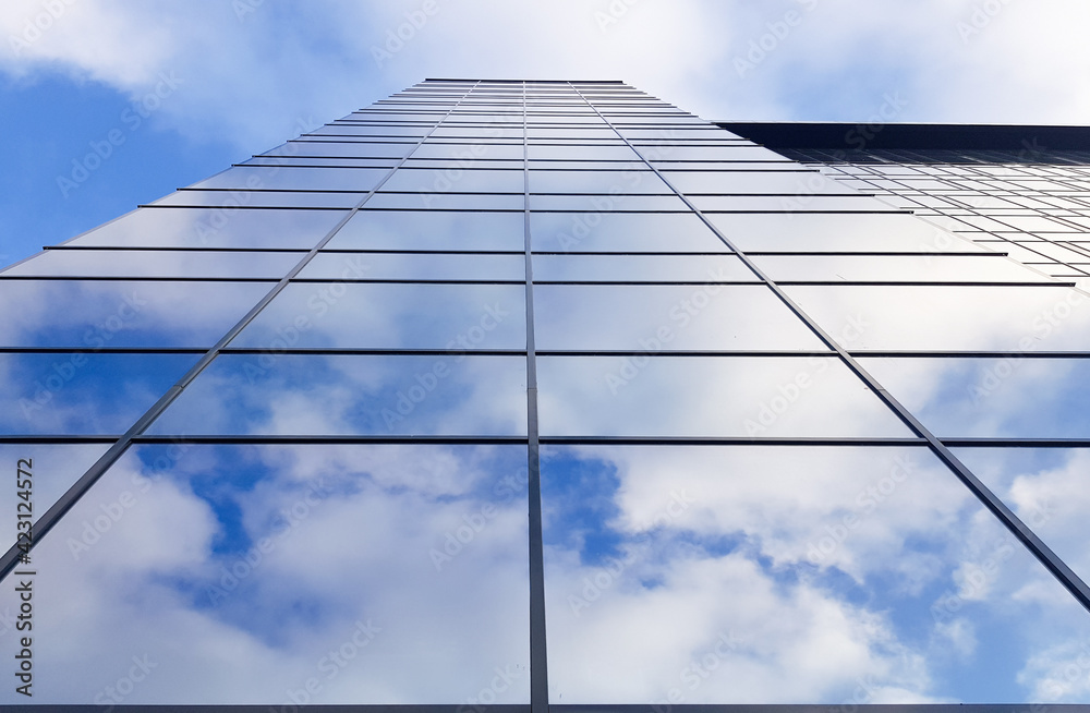 View of a modern glass skyscraper. Reflection of a cloudy blue sky in a glass skyscraper View of a modern glass skyscraper. Reflection of a cloudy blue sky in a glass skyscraper