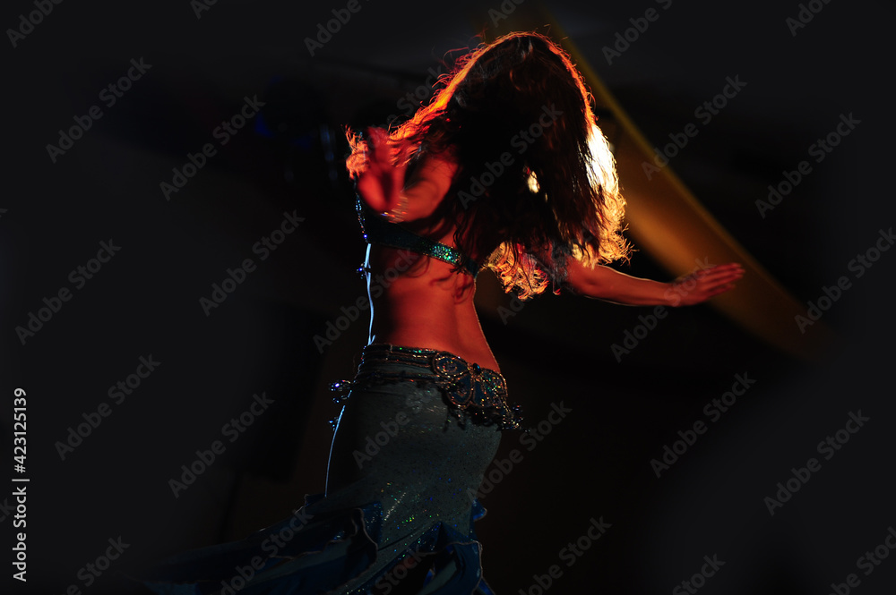 Silhouette view of a solo belly dancer dancing in the dark