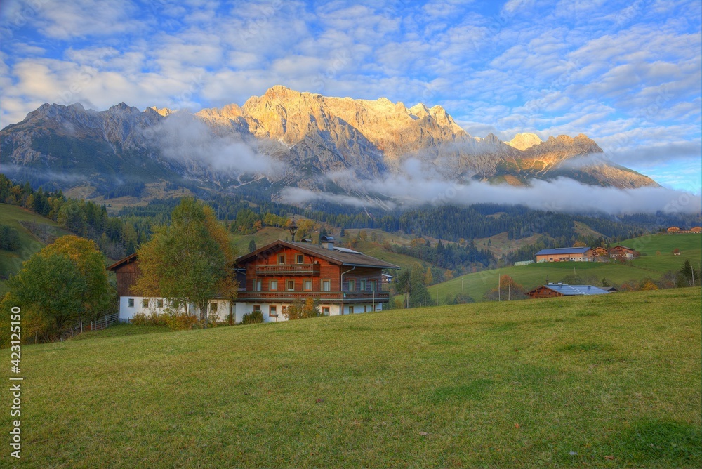 Country houses at foothills of a rocky mountain range lighted up by golden sunlight at sunset~Sunset scenery of a beautiful village by Hochkonig Mountains between Dienten & Muhlbach, in Austria Europe