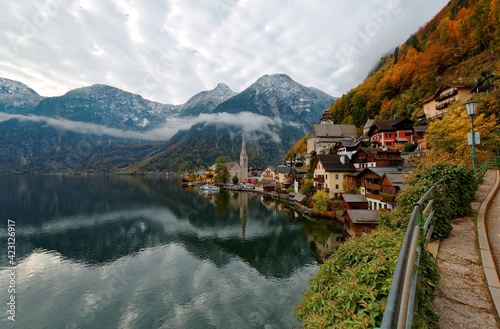 Scenic postcard view of famous Hallstatt, a peaceful village by Hallstatter Lake in Austrian Alps, with a boat cruising on lake & reflections of mountains, village houses & dramatic sky on the water