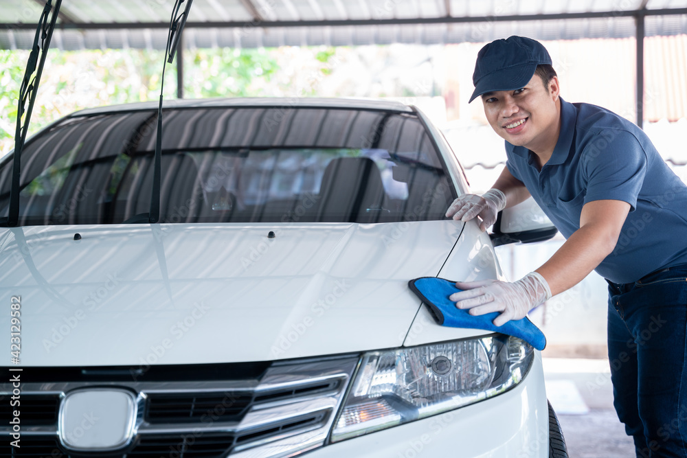 Fototapeta premium happy asian man in uniform holds the microfiber in hand and polishes the car, Car wash service concept.