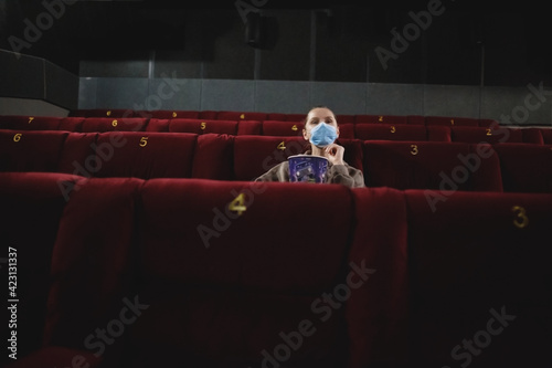 young woman in medical mask eating popcorn sitting in the cinema