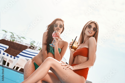 Summer is here, let’s give a big cheer! Attractive girls sitting by the pool, having fun © Friends Stock