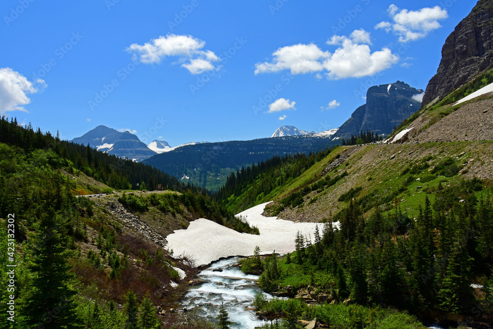 scenic view from siyeh bend of snow field, river, forest, peaks, and glacial valley  in early summer along the going-to-the-sun road in glacier national park, montana
