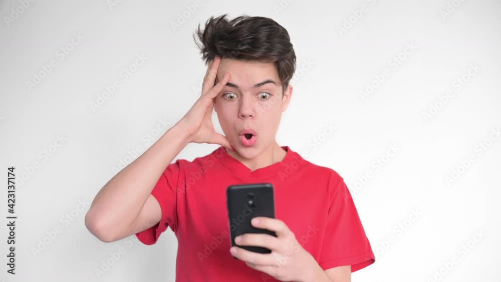 Boy is on his smartphone and getting shocked. White background Boy is on his smartphone and getting shocked. White background