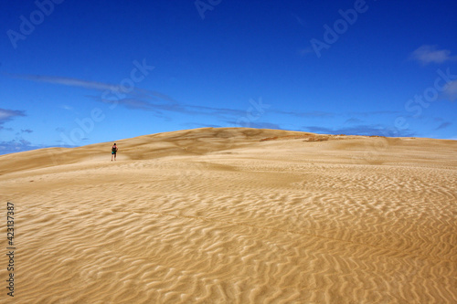 Lonely man silhouette walking in the dunes, blue sky background