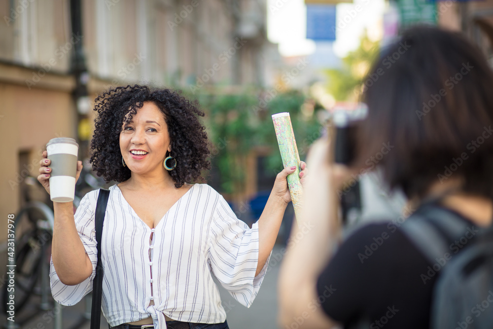 Smiling woman standing on the street with cup of coffee. Woman taking photo of her friend.