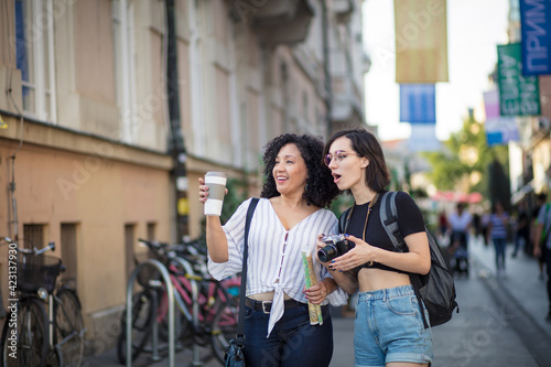Smiling women standing on the street with cup of coffee and camera in hands. © liderina