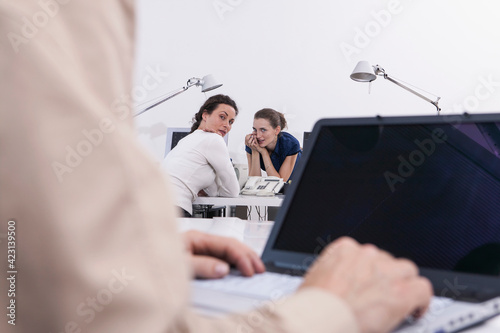 Businesswomen gossiping about colleague in office
 photo