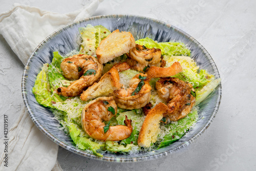 Classic caesar salad with grilled shrimps on gray background.