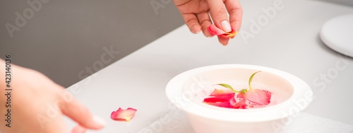 Beautician's female hands preparing manicure bath with red and pink roses petals on the table in spa