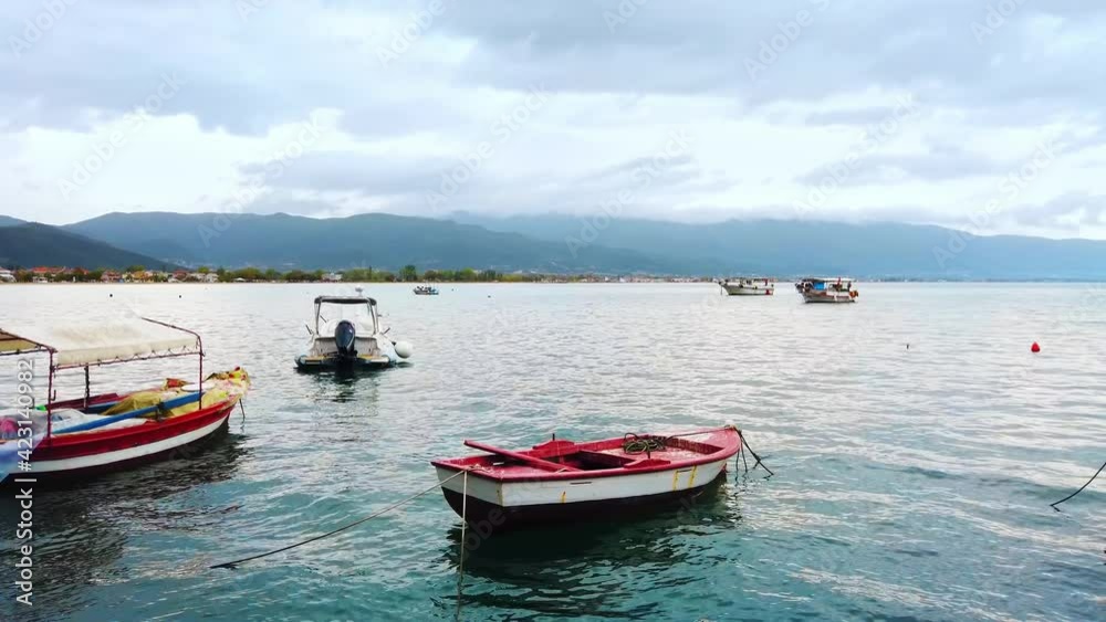 Moored boats on the shore of the Aegean sea, town and hills on the background, cloudy sky in Stavros, Greece Moored boats on the shore of the Aegean sea, town and hills on the background, cloudy sky in Stavros, Greece
