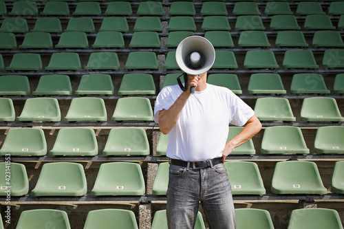 Man using bullhorn among green stadium seats
