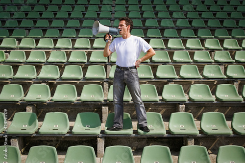 Man yelling into bullhorn on green stadium seats
