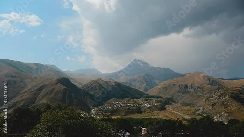 Beautiful nature landscape timelapse in georgian mountains Kazbegi, Stepantsminda.Moving clouds from the horizon. View from above to the amazing valley and range. Sun llights on the hills and trees. photo