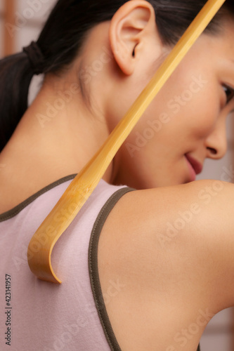Close up young woman using wooden back scratcher
