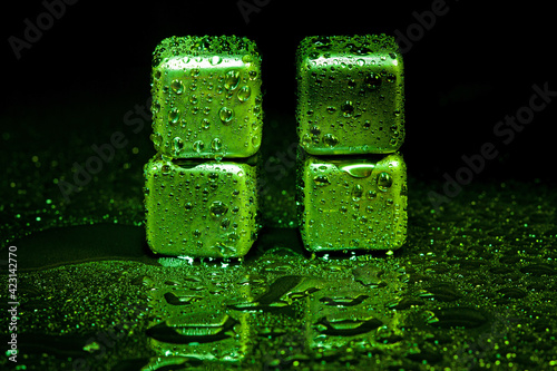 Green stainless steel cubes simulating ice for cooling drinks on a black surface with a reflection.