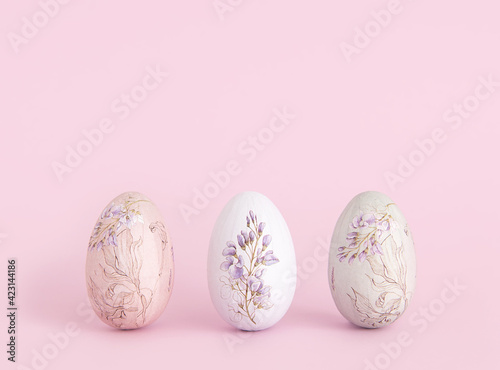 Three Easter eggs decorated with a floral pattern on a pink background. Happy Easter card with copy space for text. Minimal style.