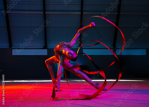 Young graceful girl gymnast isolated over colored background in neon light