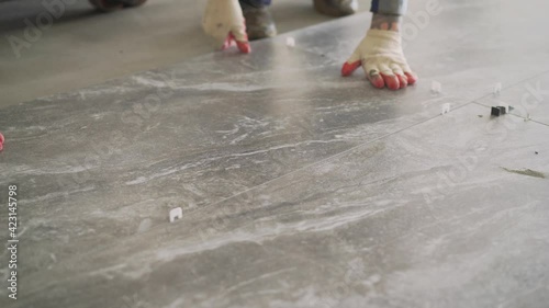 Laying floor ceramic tile. Renovating the floor. Construction workers laying tile over concrete floor using tile levelers, notched trowels and tile mortar.