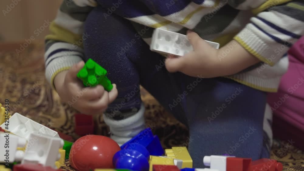 The child is played with toys. Little boy assembles the constructor on the bed. Multi-colored toys. Small baby details. Self-isolation of the baby in the house. Colored children's socks and tights The child is played with toys. Little boy assembles the constructor on the bed. Multi-colored toys. Small baby details. Self-isolation of the baby in the house. Colored children's socks and tights