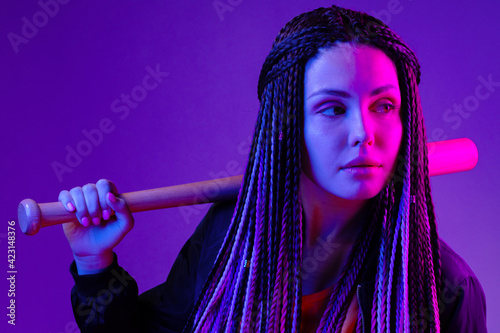 Young woman with afro braids holding a bit on a shoulder in neon lught photo