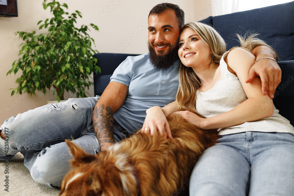 Young loving couple relaxing in living room with their dog pet - obrazy, fototapety, plakaty 