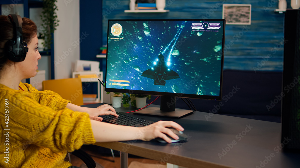 Naklejka premium Concentrated gamer playing first-person space shooter online video game on powerful personal computer spending loisure time at home. Esport cyber performing during gaming tournament