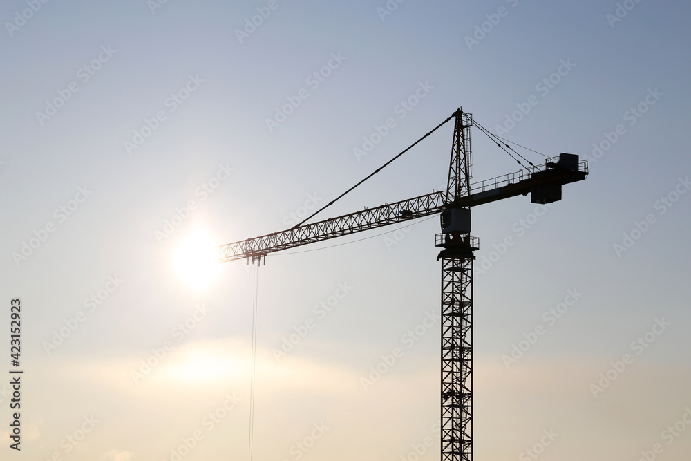 Silhouettes of tower crane against sunshine. Housing construction