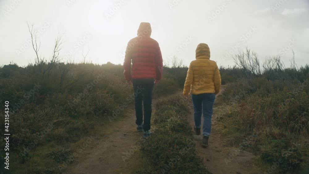 Two friends or couple in colourful puffy jackets walk on morning hike on gravel road. Autumn or winter activity outdoors Two friends or couple in colourful puffy jackets walk on morning hike on gravel road. Autumn or winter activity outdoors
