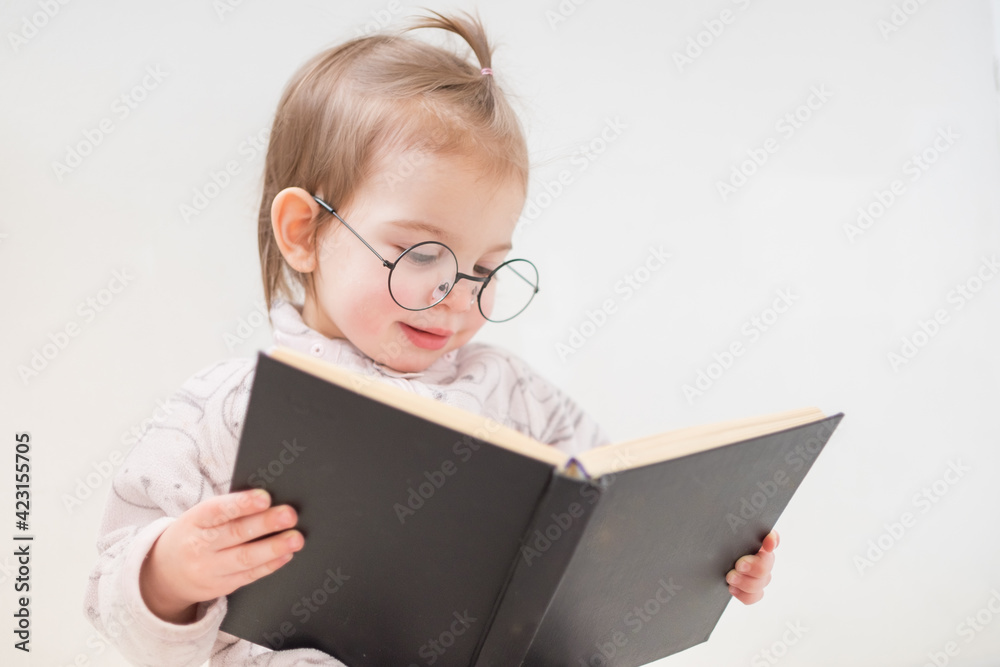 Cute toddler girl in glasses reading book on white background Cute toddler girl in glasses reading book on white background