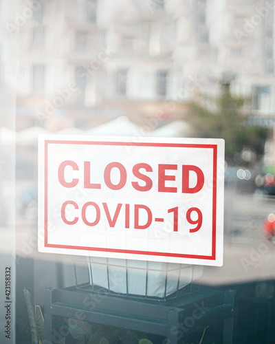 Close up on closed sign in the window of a shop with inscription Closed due to Covid-19. Stores, restaurants, offices, other public places temporarily closed