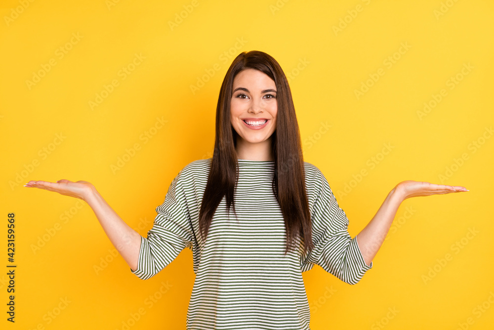 Photo of positive adviser lady two hands hold empty space look camera wear striped shirt isolated yellow background Photo of positive adviser lady two hands hold empty space look camera wear striped shirt isolated yellow background