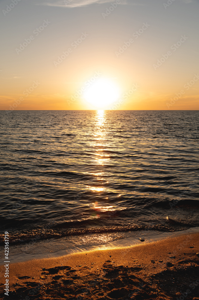 Vertical shot of golden sunset on a deserted beach with waves on the sea surface